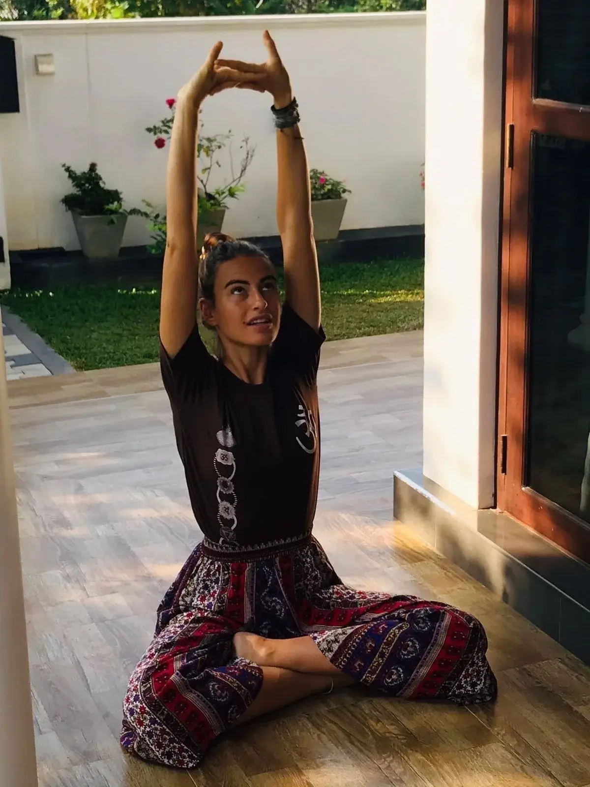 An adult visitor seated with arms raised during a yoga moment on the veranda